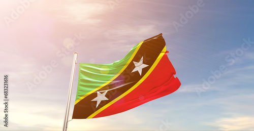 Saint Kitts and Nevis national flag waving in beautiful sky. The symbol of the state on wavy silk fabric.