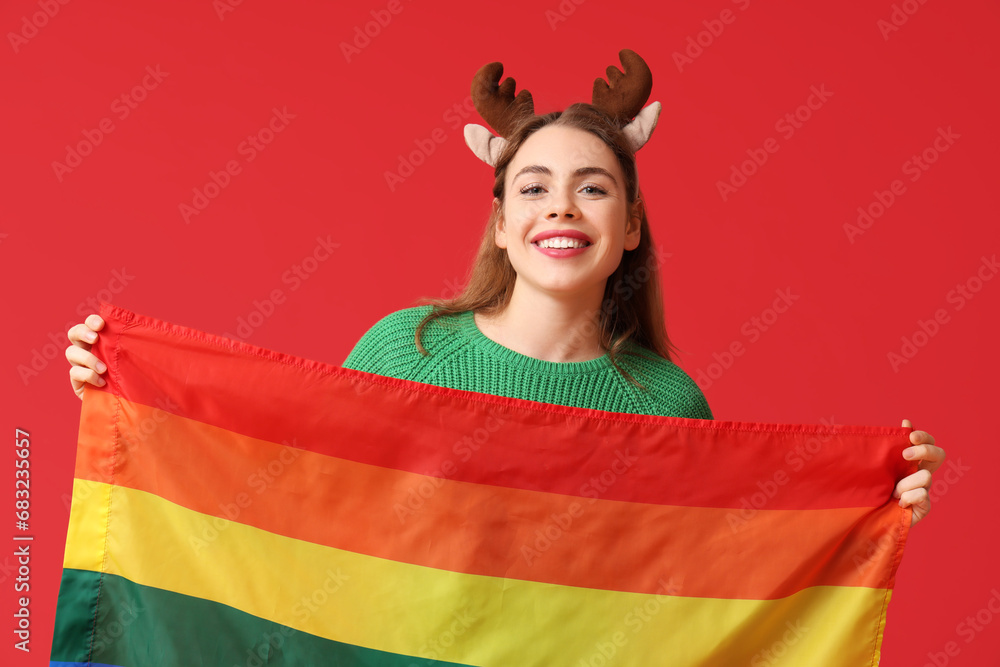 Young woman in reindeer horns with LGBT flag on red background Young woman in reindeer horns with LGBT flag on red background