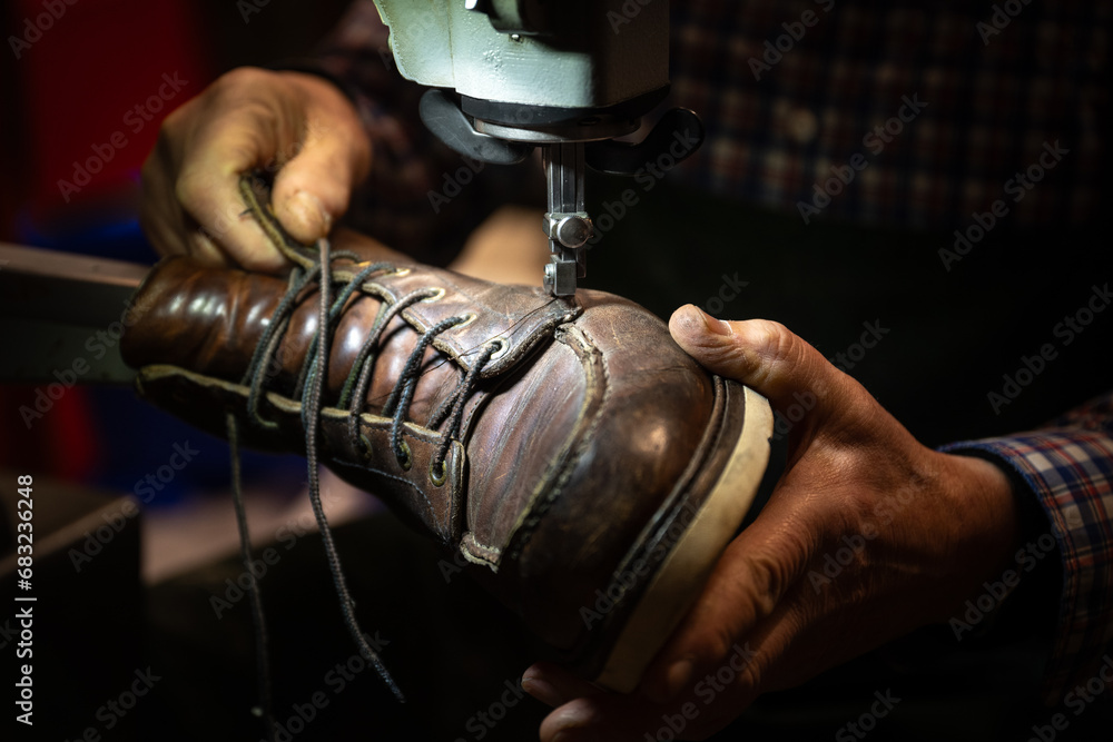 Schuster, der einen alten Schuh in den Händen hält und an der Nähmaschine reparieren will - obrazy, fototapety, plakaty 