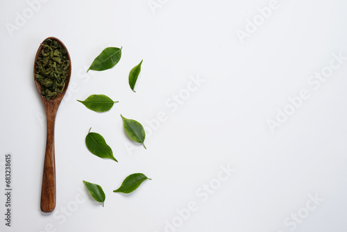 Dry tea with fresh green leaves in wooden spoon, isolated on white background. Top view, flat lay. Space for text.