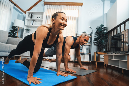 Athletic and active senior couple doing exercise on fit mat with plank climbing together at home exercise as concept of healthy fit body lifestyle after retirement. Clout