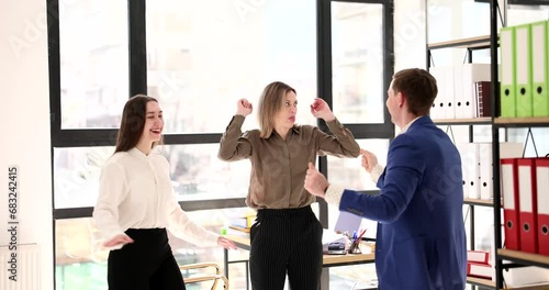 Woman looks in surprise at happy joyful successful colleagues and starts dancing with them. Teamwork and successful business team photo