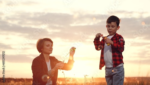 Mother and son blow soap bubbles together at sunset in middle of field