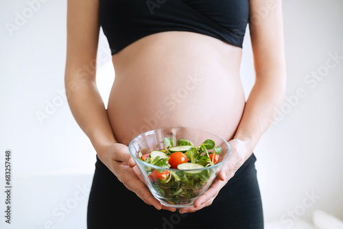 Pregnant woman's belly and vegetable salad. Prenatal nutrition during pregnancy.
