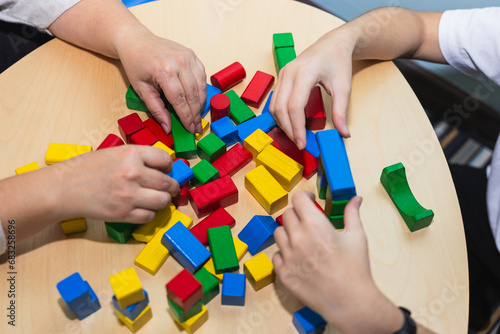 Top view of the hands of an adolescent patient and her psychotherapist working with colorful wooden toy blocks in therapy. Concept of therapy and mental health photo