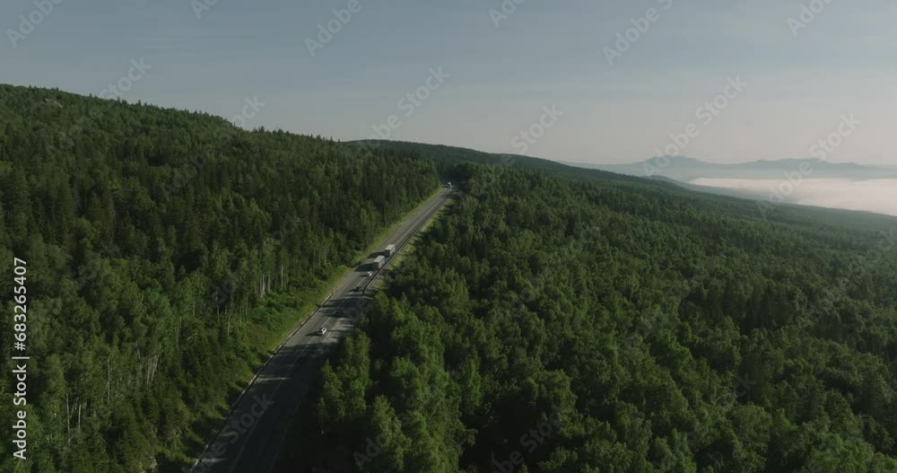 Two Semi Trucks with white trailer and cab driving, traveling alone on dense forest mountain winding road, highway perspective view follow vehicle aerial footage. Freeway trucks traffic Two Semi Trucks with white trailer and cab driving, traveling alone on dense forest mountain winding road, highway perspective view follow vehicle aerial footage. Freeway trucks traffic