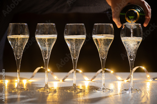 New year party, pouring of brut champagne bubbles cava or prosecco wine in tulip glasses with garland  lights on background photo