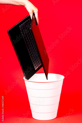 Black laptop in a trash bin on a red background isolated