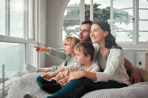 Parents, children and relax by window, happy and pointing with view, bonding and love with in family house. Father, mother and kids with conversation, talking and smile on bean bag, wow face and home