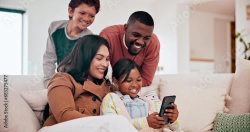 Happy, phone and children with parents on a sofa in the living room of modern family home. Laughing, having fun and young kids watching video on cellphone with interracial mother and father in lounge photo