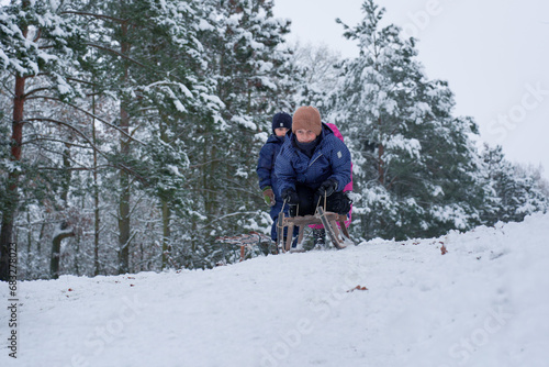 Children zooming down a snowy hill on an old-fashioned wooden sled, pine forest covered in snow on background, Sibling Bonding in winter sledding adventure