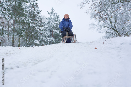 A happy child slides down a snowy hill on a wooden sled, winter fun during the holidays.