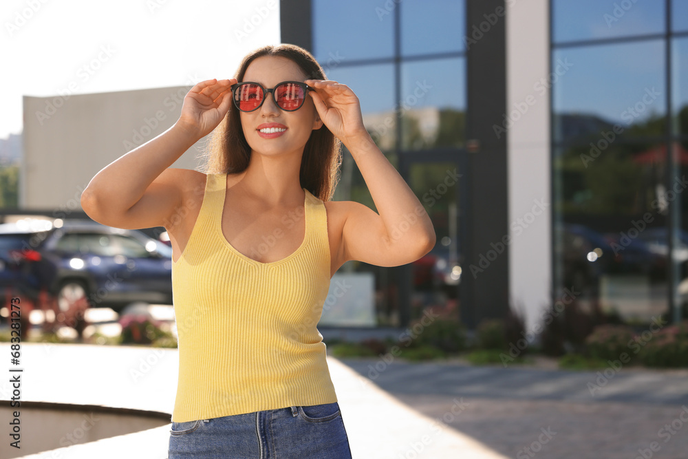 Beautiful smiling woman in sunglasses on city street, space for text