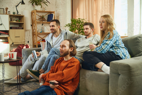 Group portrait. Guys and girl sitting in living room and spending all time watching new films with an exciting, unexpected plot.