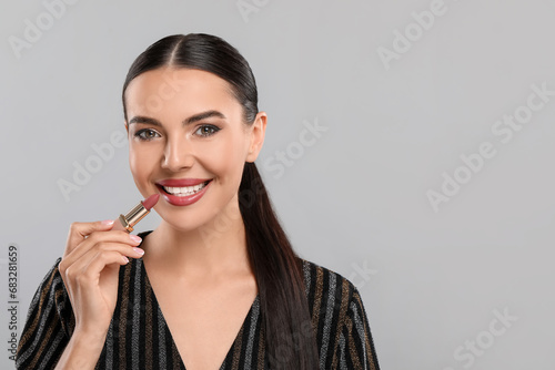 Everyday makeup. Beautiful woman applying lipstick on light grey background, space for text