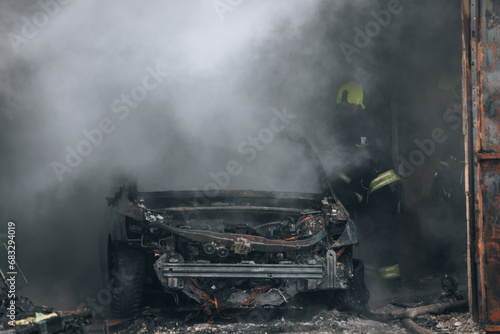 Firefighters extinguish a burning car in a garage. Burnt car. Rescuers. Strong smoke. Emergency. Insurance case.