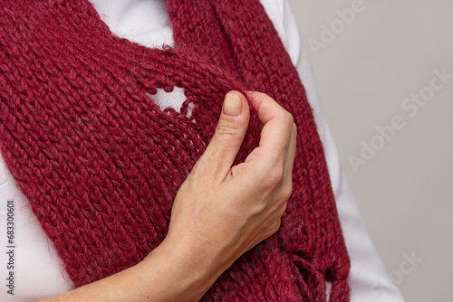 Woman hand holding knitted thing with hole made by moth