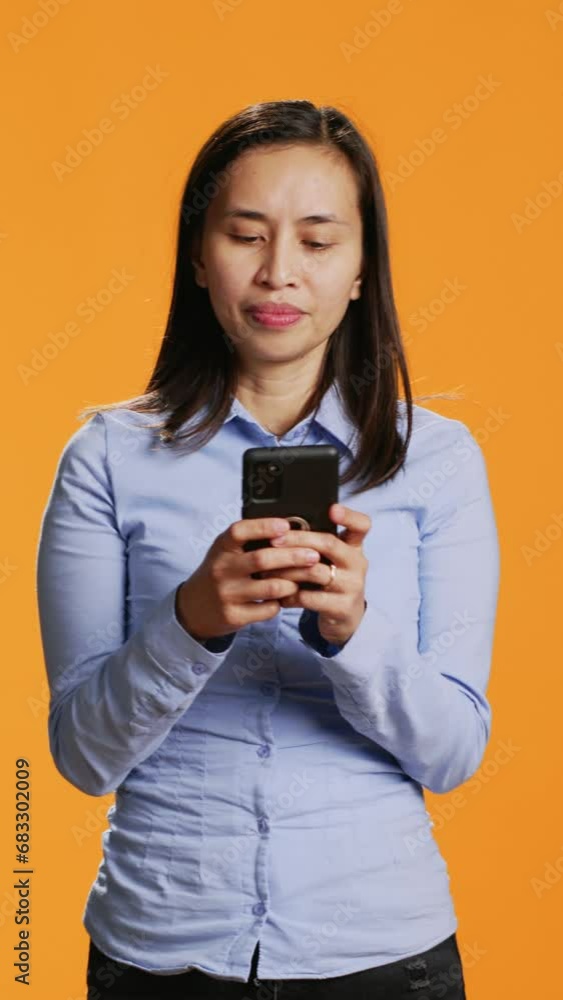 Vertical Video Young person texting messages on mobile device in studio, browsing through social media app and talking to friends online. Modern smiling woman using sms and texts for communication. Vertical Video Young person texting messages on mobile device in studio, browsing through social media app and talking to friends online. Modern smiling woman using sms and texts for communication.