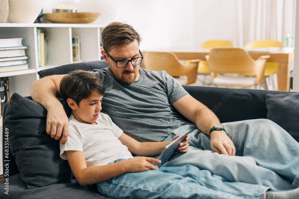 Father and son sitting together on a couch and watching motion picture on tablet. Father and son sitting together on a couch and watching motion picture on tablet.