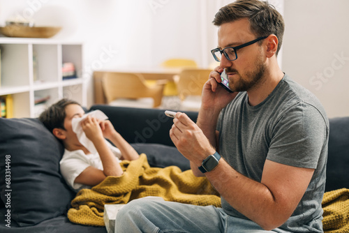 Worried father is calling a pediatrician because his son has a flue.