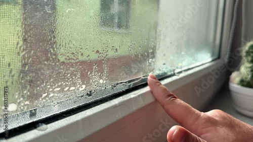 Close-up of condensation on PVC white plastic window, woman drawing on the glass, selective focus. Indoor humidity level concept.