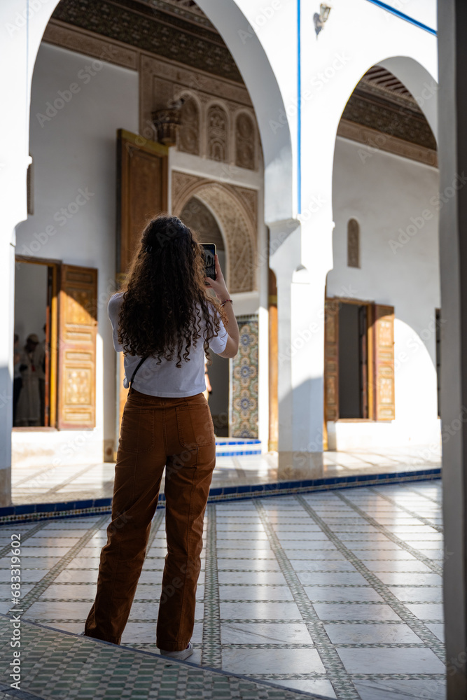 (Selective focus) Stunning view of a tourist taking a photo at the Bahia Palace during a sunny day. The Bahia Palace in Marrakech is an impressive example of Moroccan architecture and design.