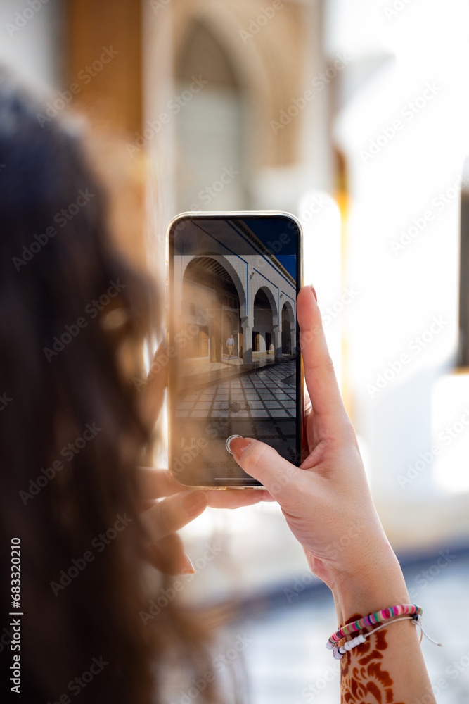 (Selective focus) Defocused girl in the foreground taking a photo at the Bahia Palace during a sunny day. The Bahia Palace in Marrakech is an impressive example of Moroccan architecture and design.