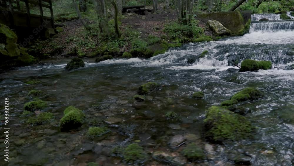 Crane shot of a mountain creek with robust water stream running through cascades and over moss-sprinkled stones and sand. Crane shot of a mountain creek with robust water stream running through cascades and over moss-sprinkled stones and sand.