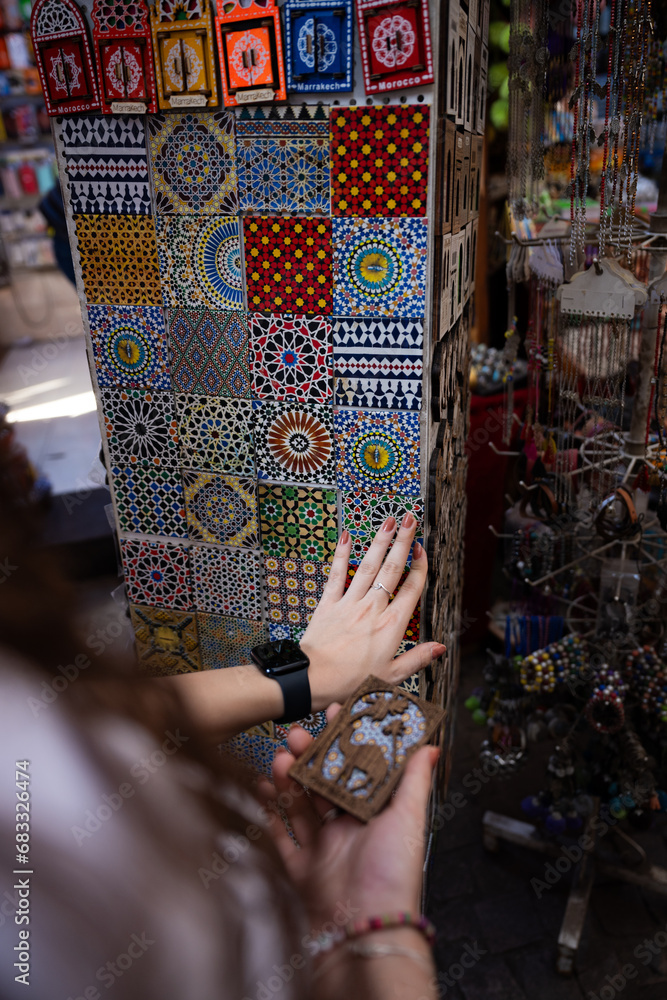 (Selective focus) Defocused girl in the foreground choosing a magnet in Marrakesh's souk, Morocco. The souks of Marrakech are the largest in Morocco and famous globally.