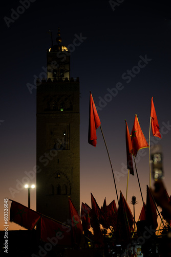 (Selective focus) Stunning view of some Moroccan flags in the foreground and defocused Kutubiyya Mosque in the background at sunset. Marrakesh, Morocco.