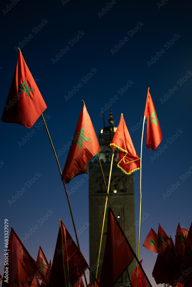 (Selective focus) Stunning view of some Moroccan flags in the foreground and defocused Kutubiyya Mosque in the background at sunset. Marrakesh, Morocco.