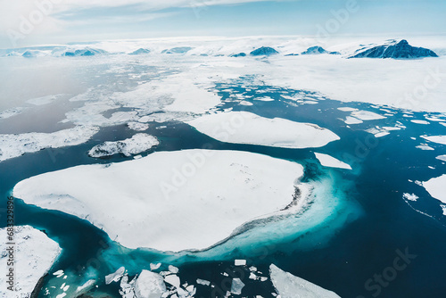 The image captures a breathtaking aerial view of icebergs floating on the ocean in the Arctic. The ice formations vary in size and shape, with some towering above the water's surface. photo