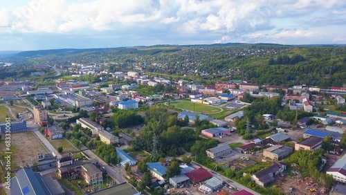 Top view of town with green forest and hills. Clip. Modern town with infrastructure in hilly forest area. Beautiful landscape of town with hilly horizon on summer day