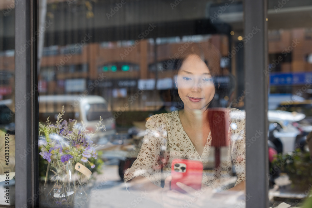 Woman use mobile phone and sit inside coffee shop with window reflection Woman use mobile phone and sit inside coffee shop with window reflection