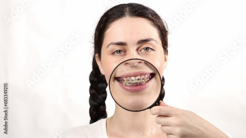 Portrait of young Caucasian smiling woman showing x-ray, magnifier glass and teeth with ligature braces. White background. Concept of orthodontic treatment photo
