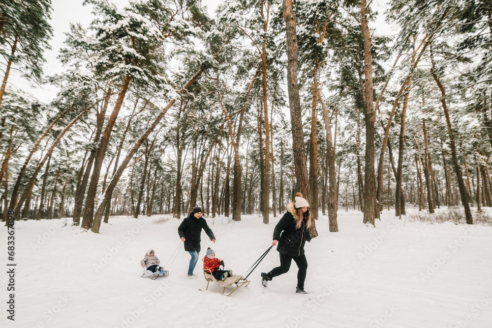 Portrait family runs and walks in snowy forest. Father, mother, daughter, son with sled in winter park. Family with two small children in winter nature. Mom, dad, kids enjoying snowfall in snowy woods