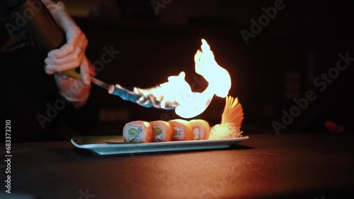 Master sushi maker makes sushi rolls from nori rice and red fish, the process of preparing Japanese food close-up, orange salmon trout fish, scorched by fire