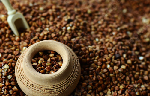 Background image of a large pile of buckwheat, in the middle of which lies a small jug and a wooden spatula for cereals