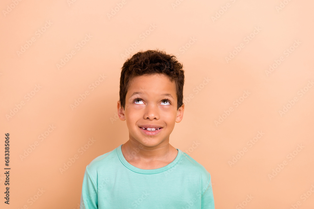 Photo of nice cute good mood boy wear turquoise trendy clothes looking up empty space isolated on beige color background Photo of nice cute good mood boy wear turquoise trendy clothes looking up empty space isolated on beige color background