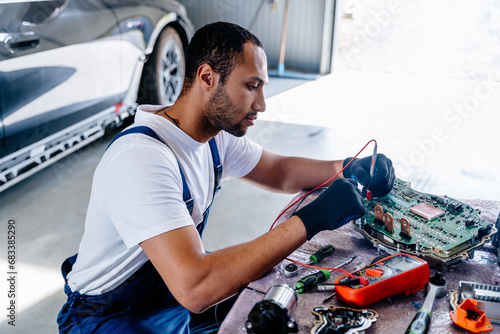 Arabian male auto mechanic examining a car engine removed from car for repair with voltmeter. Electronic Control Unit (ECU) of modern electric car. photo