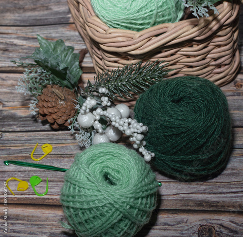 green wool yarns in basket and on the wooden table, crochet markers,decoraive christmas branch.