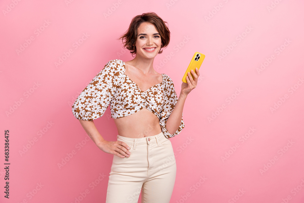 Photo of stunning skinny positive girl toothy smile hold use smart phone chatting isolated on pink color background Photo of stunning skinny positive girl toothy smile hold use smart phone chatting isolated on pink color background