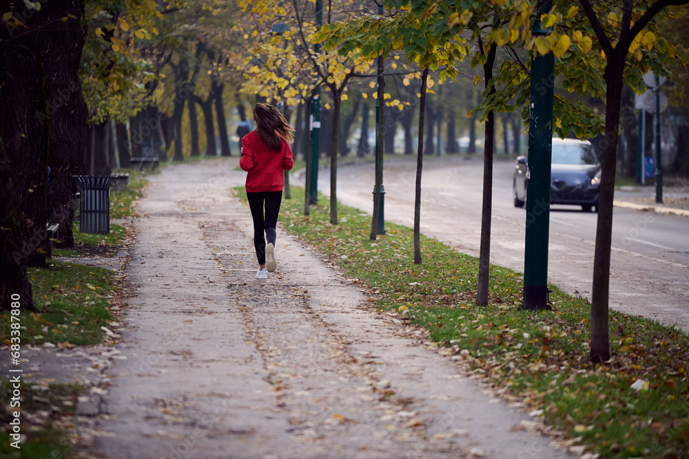 Young beautiful woman running in autumn park and listening to music with headphones on smartphone