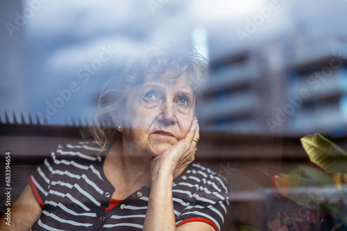 Portrait of senior woman looking through window 
 photo