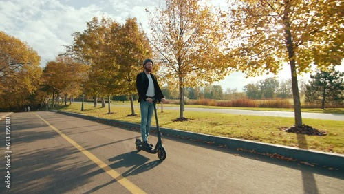 Joyful guy in protective helmet in casual outfit using eco-friendly transportaion method exploring the territory of park in sun glare, driving on the path. High quality 4k footage photo