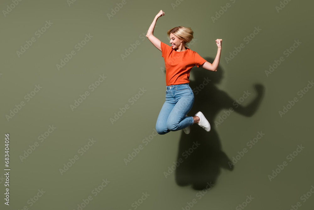 Full body photo of woman in orange t shirt denim jeans raised fists up shopaholic celebrate black friday isolated on khaki color background Full body photo of woman in orange t shirt denim jeans raised fists up shopaholic celebrate black friday isolated on khaki color background