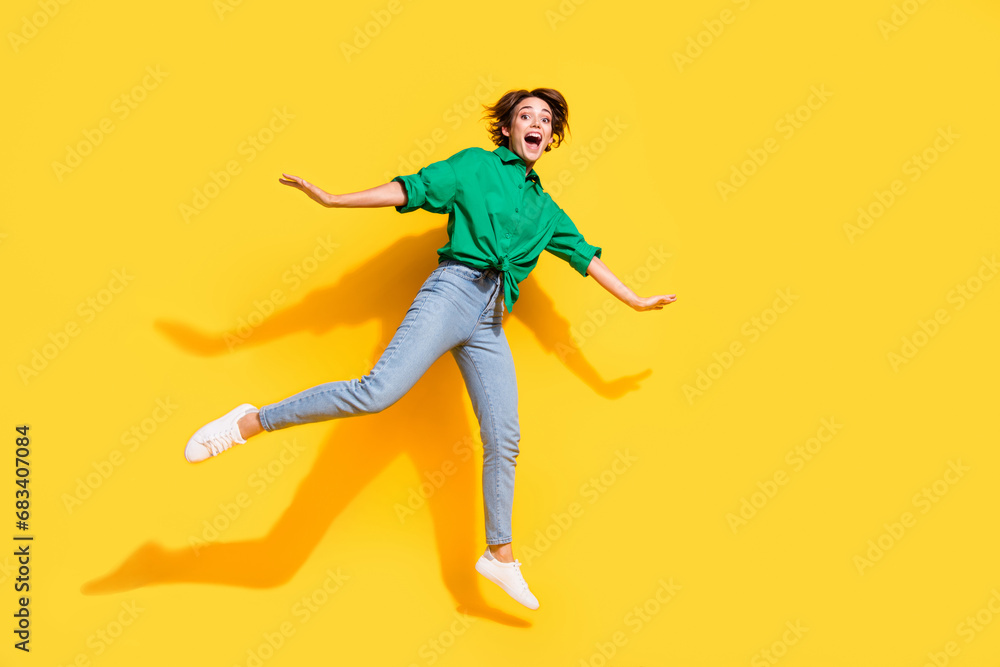 Full length photo of excited funky girl dressed green shirt jumping high empty space isolated yellow color background