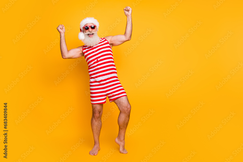 Full length photo of good mood dreamy senior guy dressed christmas swimwear sunglass rising fists empty space isolated yellow color background Full length photo of good mood dreamy senior guy dressed christmas swimwear sunglass rising fists empty space isolated yellow color background