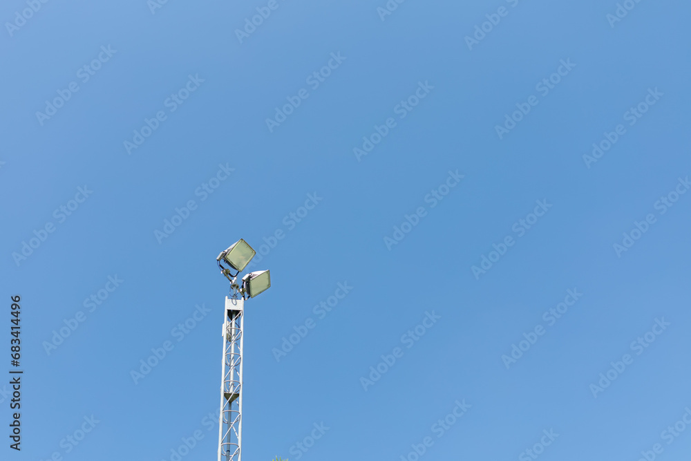 Tall spotlight pole against the background of a blue sky. Tall spotlight pole against the background of a blue sky.
