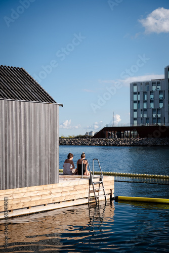Two Women Relaxing on Wooden Dock at Urban Harbor Swimming Area in Summer